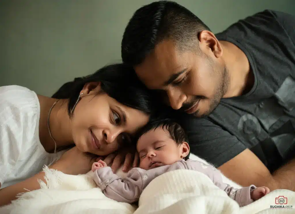 Newborn photo session capturing parents lovingly admiring their peacefully sleeping baby, photographed by Ruchika Jain Photography.